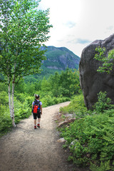 girl with backpack walking in the woods with big boulder