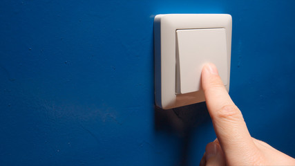 Human hand turn off a power button on a blue wall - side view