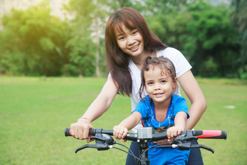 Asian mother and her daughter ride a bicycle together.