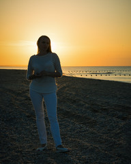 Silhouette of beautiful woman in white pants and white jacket in the background of the sunset sea.