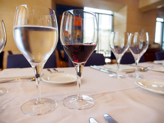 Close-up wide angle of a glass of water and red wine on a set table with plates and silverware before a gala dinner. Valencia, Spain. Travel and gourmet cuisine concept.