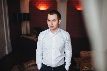 Fototapeta premium A handsome confident young man standing seriously in a white shirt in house.