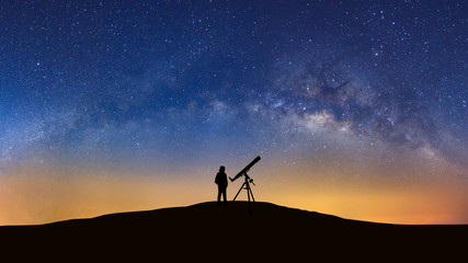 Fototapeta premium Silhouette of a standing man with telescope watching the wilky way galaxy