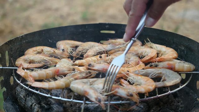 Hand turns the shrimp on grill. Grilling shrimps on barbecue. Grilled seafood on bbq