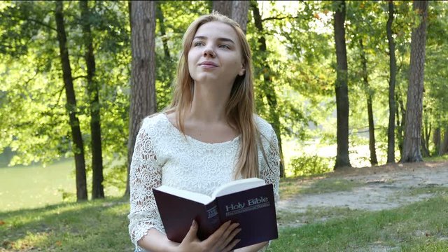 4k. Bible  and attractive girl in sunny park. Christian team shot