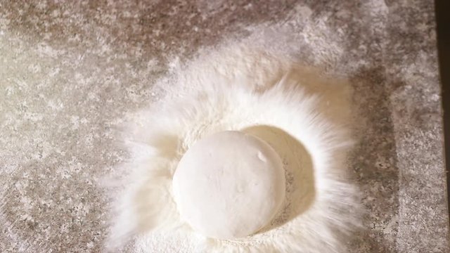 The process of cooking pizza by a cook in a restaurant. A piece of raw pizza dough falls on the table into flour in slow motion. 4K.