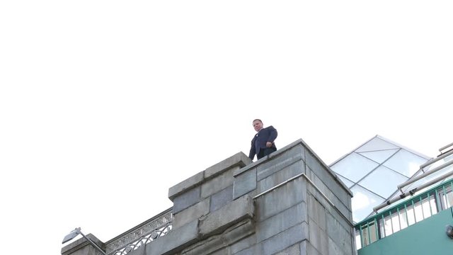 The man walks to the edge of the bridge and looks down. Shooting from the ground.