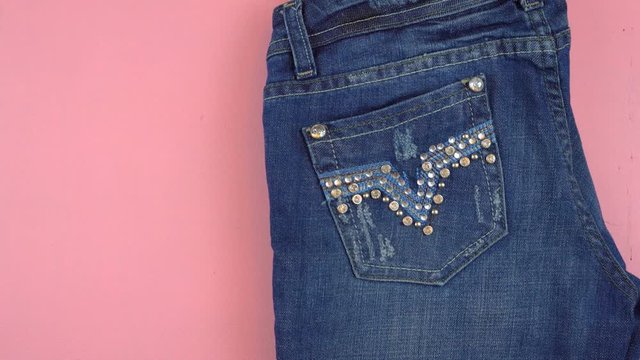 Woman laying out jeans, pink high heels, lipstick and necklace overhead on pink wood table, time lapse.