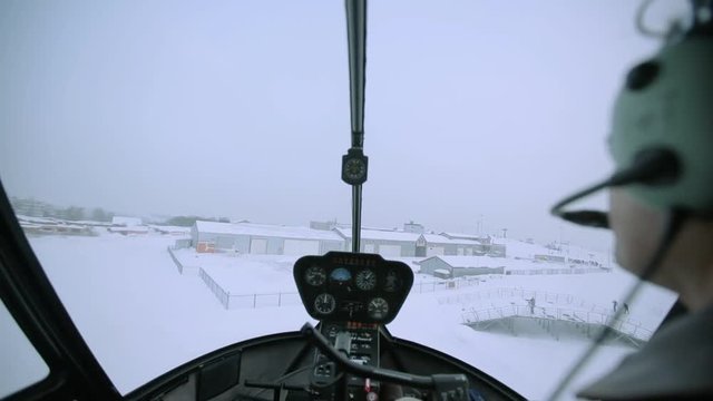 Helicopter cockpit view during snowy landing, showcasing pilot's perspective, with snow-covered landscape and airport runway visible, emphasizing aviation challenges in winter conditions