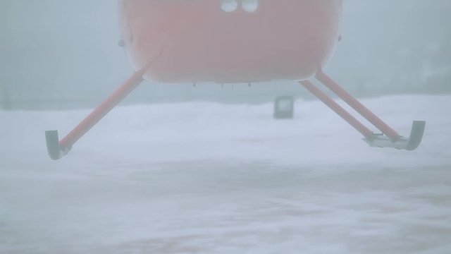 A red helicopter takes off in a snow-covered field.