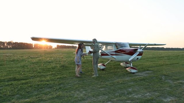 The girl and the man approach the plane and greet the pilot.