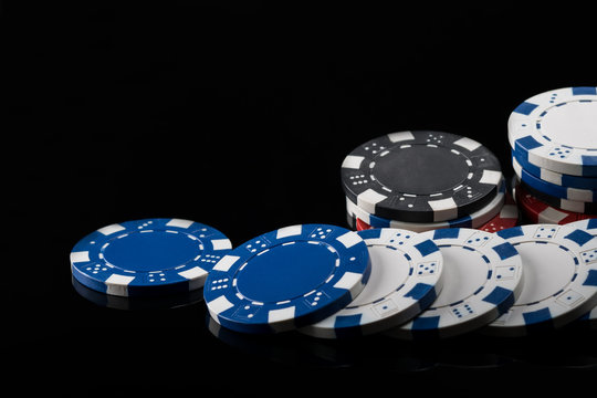 poker chips of different colors, scattered in length on a black reflective surface