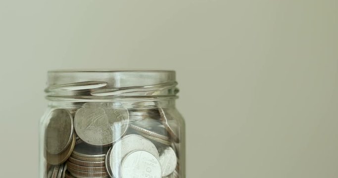 Close up Money coin falling into glass jar , money saving , donation or business financial growth concept , 4K Dci resolution