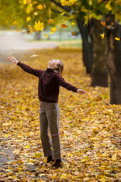 Young teenage girl throws up an armful of yellow leaves in an autumn park