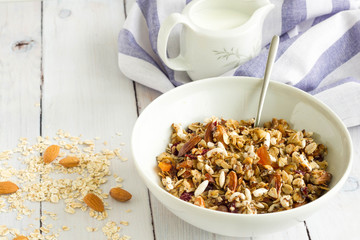 Homemade breakfast with oats, nuts and dried fruits. A cup of milk and blue table cloth in the background, natural colors.