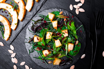 Warm pumpkin salad with mixed leaf of arugula, chard, in on black slate plate on black background. Grilled pumpkin. Top view