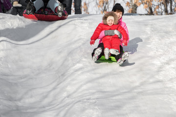 Happy mother and her daughter enjoying a sledge ride down the hill