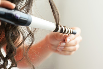 Hairstylist curling hair client in hairdressing salon