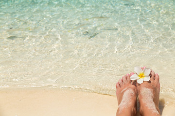 Bare female feet with single white frangipani flower, in the water of the sea with small tropical fish surrounded, holiday concept.