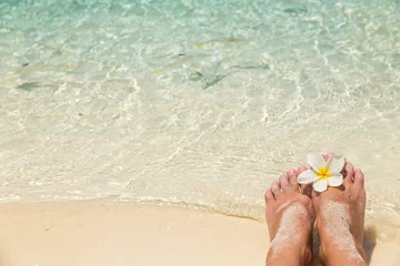 Zelfklevend Fotobehang Bare female feet with single white frangipani flower, in the water of the sea with small tropical fish surrounded, holiday concept. © 18042011