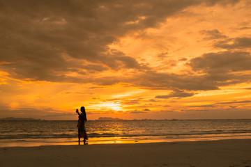 Golden scene on the beach at sunset. Tourist girl sefie herself with sunset at the coast.