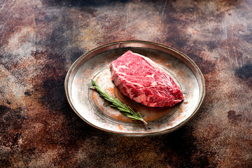 Raw steak ribeye with rosemary on a metal plate