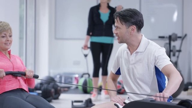  Mature woman working out on rowing machine with personal trainer