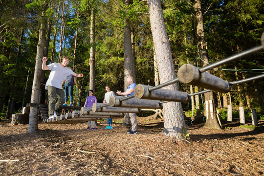 Friends Watching Man Crossing Log Bridge In Forest - Powered by Adobe