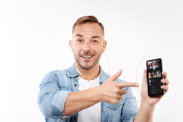 Cheerful young man pointing at phone with music player