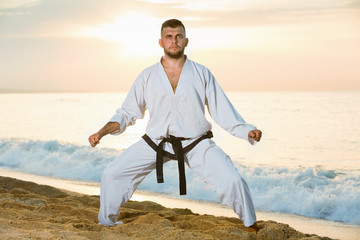 Guy doing karate poses at  sunset sea shore