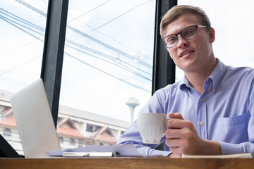 businessman hold coffee cup at workplace. young man smile & look at camera at office. employee take a break after work.