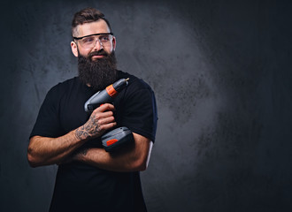 A man holds a drill over grey background.