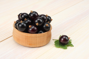 black currant in wooden bowl with green leaf on white wooden background