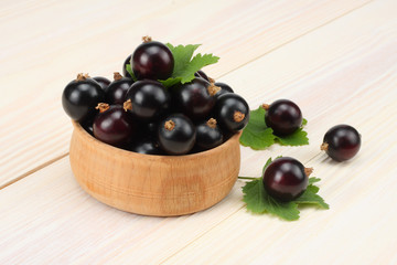 black currant in wooden bowl with green leaf on white wooden background