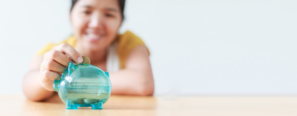 Asian woman putting money coin in to clear piggy bank metaphor saving money financial ratio for web banner and header design