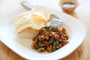stir fried pork and basil with rice and egg on wood background thai food