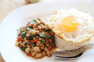 stir fried pork and basil with rice and egg on wood background thai food