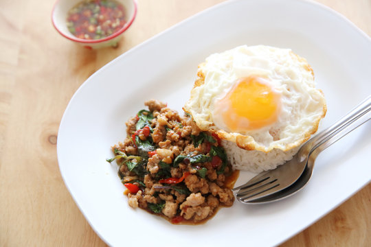 stir fried pork and basil with rice and egg on wood background thai food