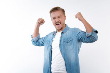 Fototapeta premium Upbeat young man raising hands with clenched fists