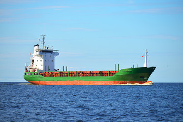 Obraz premium Unloaded green general cargo ship sailing calm sea near a port in Latvia