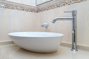 beautiful white bathroom sink with a elegant faucet on a background of beige marble tiles