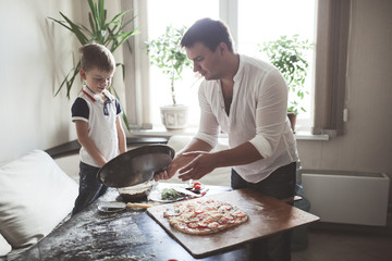 dad and son are preparing pizza in cozy kitchen