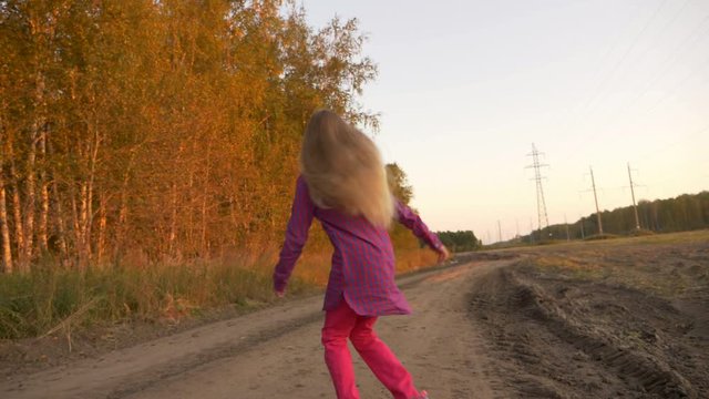Young caucasian girl running jumping by country road. White blonde long hair girl jumping outdoors.