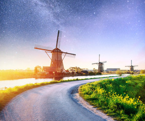 Colorful spring night with traditional Dutch windmills canal in Rotterdam. Wooden pier near the lake shore. Holland. Netherlands. Fantastic starry sky and the milky way
