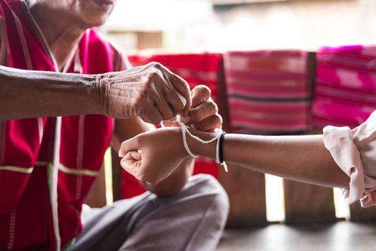 Unidentified elder man from Karen ethnic hill tribe minority tie guest's wrist for blessing in tying ceremony
