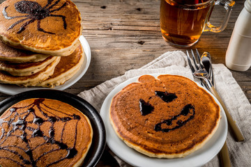 Ideas for breakfast are Halloween, food for children. Pumpkin pie pancakes decorated with chocolate syrup in a traditional style - spider web, spider, jack lantern. On wooden rustic table, copy space