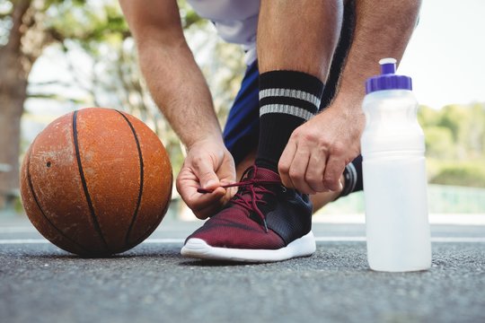 Low section of basketball player tying shoelace - Powered by Adobe