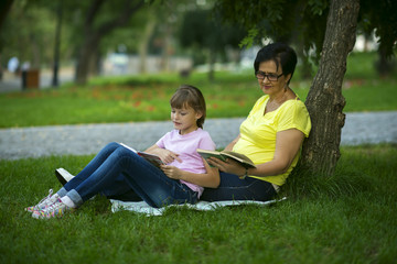 Grandmother and granddaughter reading books sitting on grass in park