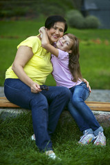Fototapeta premium Granddaughter embraces grandmother, sitting on bench in park close-up