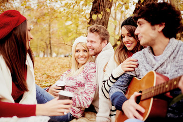      Friends having a good time in park at autumn/ singing and playing guitar 